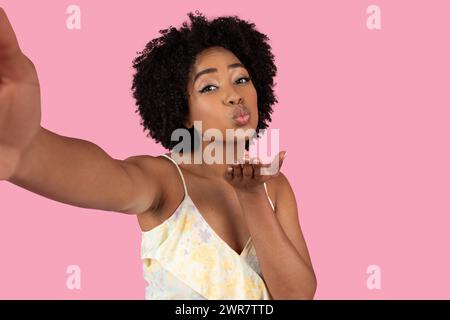 Eine charmante afroamerikanische Frau mit natürlichem Afro-Haar weht spielerisch einen Kuss Stockfoto