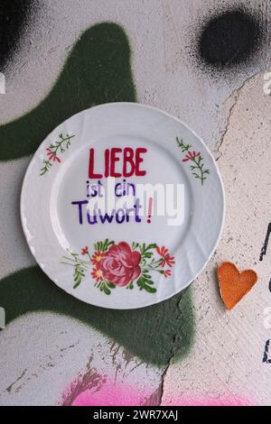 Street Art in der Körner Straße: Ein Teller klebt an einer Wand mit dem Spruch Liebe ist ein Tuwort ! Daneben hat jemand auf französisch geschrieben Stockfoto