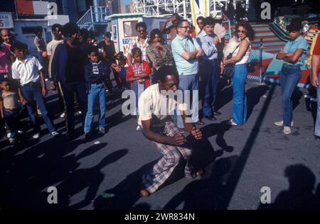 Coney Island 1980er Jahre USA. Ein Afroamerikaner in karierten Hosen, damals modisch, tanzte allein auf der Straße. Eine Menge Zuschauer beobachtet seine Bewegungen. Coney Island, Brooklyn, New York, USA 27. Juni 1981. Stockfoto