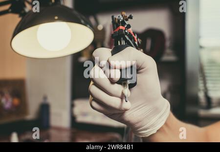 Tattoo Master Schutzhandschuhe halten die Tattoo-Maschine mit schwarzer Tinte. Nahaufnahme. Stockfoto