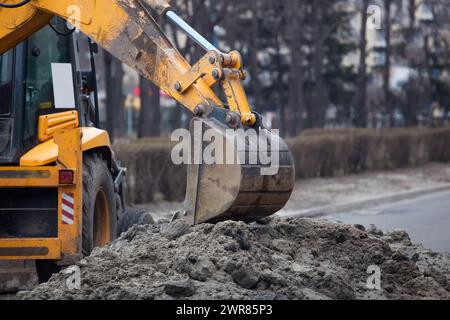 Ein großer gelber Bagger steht in der Mitte der Straße in der Nähe des Grabens. Stockfoto