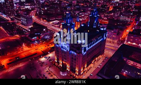 Nächtlicher Blick auf ein beleuchtetes historisches Gebäude inmitten von Stadtstraßen mit lebhaften roten Verkehrswegen in Liverpool, Großbritannien. Stockfoto