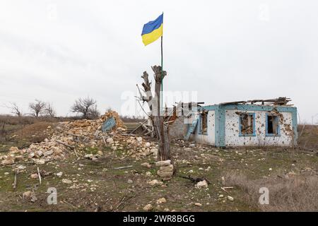 Region Mykolaiv, Ukraine. März 2024. Eine ukrainische Flagge ist an einem beschädigten Baum vor dem Hintergrund eines Wohngebäudes in einem Dorf in der Region Mykolajew angebracht, das von russischen Truppen vollständig zerstört wurde. Eine typische Szene eines ukrainischen Dorfes in der Region Mykolajew, wie in anderen Regionen der Ukraine nach der Besatzung und in der Nähe der Frontlinie. Regelmäßige Beschießung und Zerstörung von Häusern von Anwohnern. (Credit Image: © Mykhaylo Palinchak/SOPA Images via ZUMA Press Wire) NUR REDAKTIONELLE VERWENDUNG! Nicht für kommerzielle ZWECKE! Stockfoto