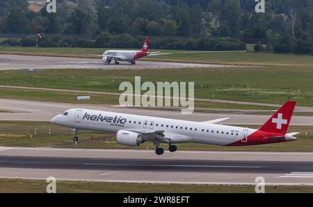 Vor einem heftigen Gewitterfront landet ein Embraer 190-E2 von Helvetic Airways auf dem Flughafen Zürich. Registrierung HB-AZI. Dahinter startete ein FL Stockfoto