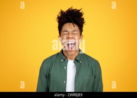 Emotionaler junger afroamerikanischer Mann, der über gelbem Hintergrund schreit Stockfoto