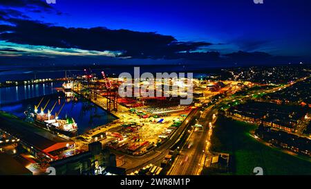 Nächtlicher Blick auf einen belebten Hafen mit beleuchteten Kränen, Frachtcontainern und Stadtlichtern, die auf dem Wasser in Liverpool, Großbritannien, reflektieren. Stockfoto