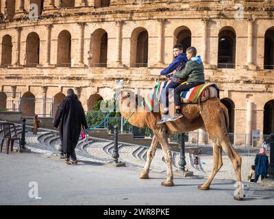 Zwei kleine Jungen machen einen Kamelritt vor dem gut erhaltenen römischen Amphitheater El Jem (Thysdrus) in Tunesien. Stockfoto