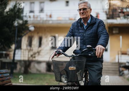 Ein fröhlicher älterer Mann mit Brille fährt in einer urbanen Umgebung Fahrrad und demonstriert einen aktiven und gesunden Lebensstil. Stockfoto