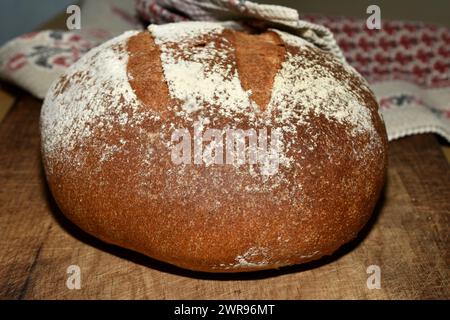 Auf dem Schneidebrett liegt rundes Brot aus Roggenmehl, das zu Hause im Ofen gebacken wurde. Stockfoto