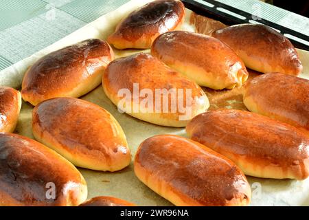 Torten mit Füllung liegen reihenweise auf einem Backblech. Stockfoto