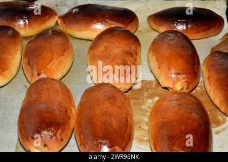 Torten mit Füllung liegen in Reihen auf einem Backblech, Draufsicht. Stockfoto