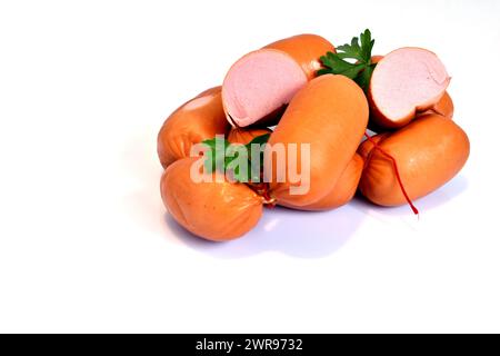 Würstchen und ein paar grüne Blätter liegen auf weißem Hintergrund. Eine Wurst wird geschnitten und ihre Füllung ist sichtbar. Stockfoto