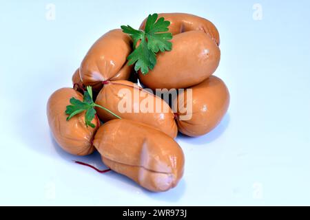 Würstchen aus Schweinefleisch und ein paar grüne Blätter liegen auf weißem Hintergrund. Stockfoto