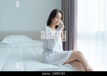 Ein schönes Mädchen sitzt Trinkwasser lächelnd glücklich im weißen Schlafzimmer trinken Wasser für Gesundheit und Schönheit befeuchten die Haut Stockfoto