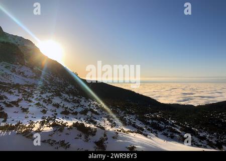 Bergsonnenaufgang über schneebedecktem Hang mit bewölktem Horizont, in der Nähe von Velické pleso in Velická dolina, oberhalb von Tatranská Polianka, hohe Tatra Stockfoto