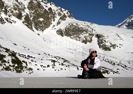 Frau, die vor schneebedeckten Bergen sitzt. In der Nähe des Hotels Sliezsky Dom, Velické pleso, in Velická dolina, oberhalb der Tatranská Polianka, hohe Tatra Stockfoto