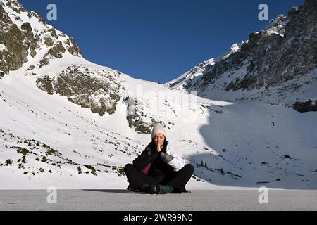 Frau, die vor schneebedeckten Bergen meditiert. In der Nähe des Hotels Sliezsky Dom, Velické pleso, in Velická dolina, oberhalb der Tatranská Polianka, hohe Tatra Stockfoto