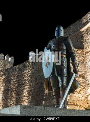 Eine Statue eines Kriegers mit zwei Schwertern und einem Helm vor einer Steinmauer Stockfoto