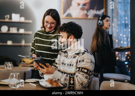 Zwei junge Erwachsene nehmen an einer gemeinsamen Arbeitssitzung Teil und tauschen sich über ein digitales Tablet in einem warm beleuchteten Café mit Bokeh-Lichtern aus. Stockfoto