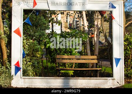 Hübsche Gartenbank, eingerahmt von einer hölzernen Pergola mit hängendem bunten Faden in Harrogate. Stockfoto