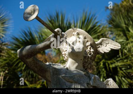 Quecksilberstatue (Hermes), die ein Horn weht, umgeben von Palmen. Stockfoto