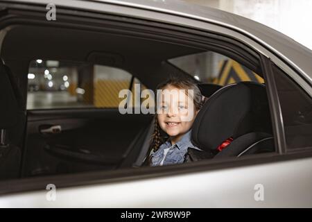 Das kleine kaukasische Mädchen sitzt auf dem Rücksitz eines modernen Autos im Kinderstuhl. Stockfoto