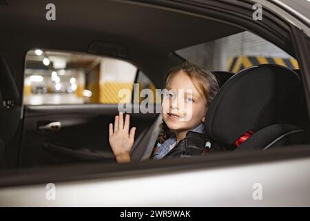 Das kleine kaukasische Mädchen sitzt auf dem Rücksitz eines modernen Autos im Kinderstuhl. Stockfoto
