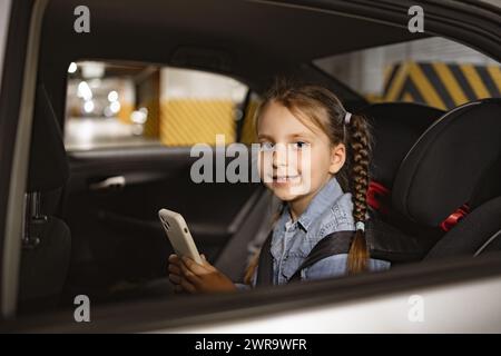 Glückliches kleines Mädchen, das auf dem Rücksitz eines modernen Autos im Kinderstuhl sitzt. Stockfoto