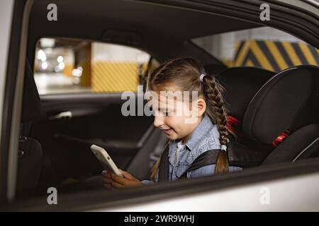 Glückliches kleines Mädchen, das auf dem Rücksitz eines modernen Autos im Kinderstuhl sitzt. Stockfoto
