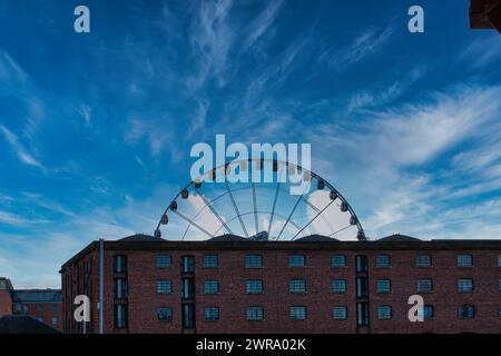 Die Silhouette des Riesenrads vor einem blauen Himmel mit schimmernden Wolken, eingerahmt von Gebäuden in Liverpool, Großbritannien. Stockfoto