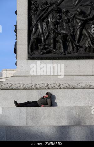 Ein Mann, der auf dem Sockel der Nelson’s Column, Trafalgar Square, London, Großbritannien, liegt. Januar 2024 Stockfoto