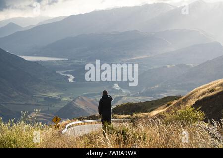 Mann fotografiert das wunderschöne Flusstal, umgeben von Bergen, mit seinem Handy, Neuseeland. Stockfoto