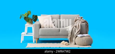 Gemütliches braunes Sofa mit Kissen, Karo, Zimmerpflanze und Hocker auf blauem Hintergrund Stockfoto