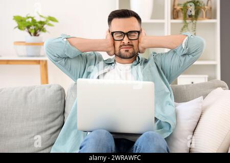 Arbeitender junger Mann mit Laptop, der zu Hause unter lauten Nachbarn leidet Stockfoto