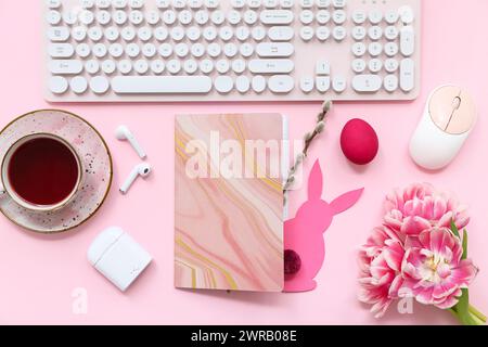 Komposition mit Notizbuch, Gadgets, Tasse Tee und Osterdekor auf rosa Hintergrund Stockfoto