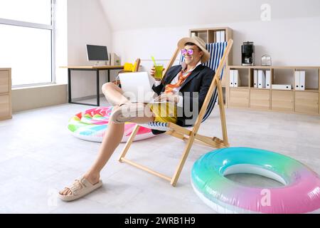 Junger Geschäftsmann mit Laptop und Cocktail bereit für den Sommerurlaub im Büro Stockfoto