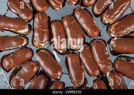 Eclairs mit Schokoladenbelag auf Servierteller. Traditionelle französische Eclairs mit Schokolade. Mini-Vanilleeclairs mit Schokoladenfrosting. Stockfoto