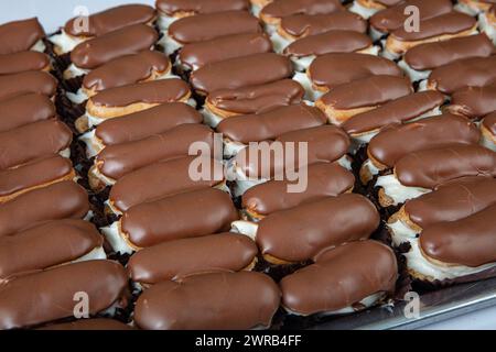 Eclairs mit Schokoladenbelag auf Servierteller. Traditionelle französische Eclairs mit Schokolade. Mini-Vanilleeclairs mit Schokoladenfrosting. Stockfoto