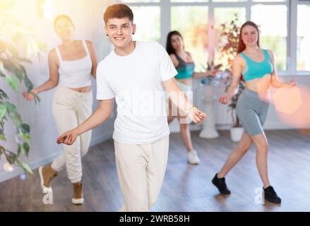 Positiver männlicher Teenager lernt Groove zu tanzen, Bewegungen im choreografischen Unterricht mit Gleichaltrigen aufzuführen Stockfoto