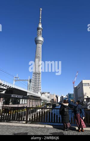 Zwei Menschen blicken an einem sonnigen Tag – Sumida City, Tokio, Japan – von einer Brücke auf den Skytree von Tokio. Am 27. Februar 2024 Stockfoto