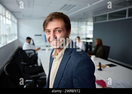 Selbstbewusster junger Geschäftsmann in Businesskleidung mit Kollegen im Büro neben dem Schreibtisch Stockfoto
