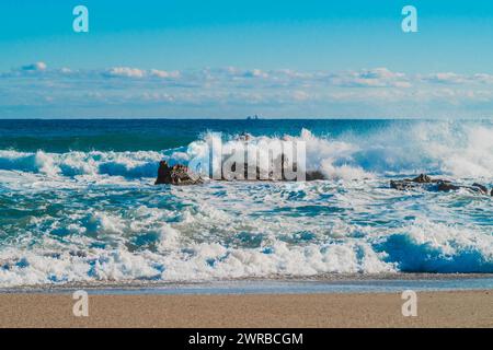 Stürzende Wellen erzeugen an einem sonnendurchfluteten Strand mit weit entferntem Horizont in Südkorea einen Sprühnebel um Felsen Stockfoto