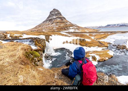 Abenteuerlustige Fotografin im Winter in Island, die am Kirkjufell-Wasserfall sitzt Stockfoto