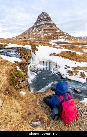 Abenteuerlustige Fotografin im Winter in Island, die am Kirkjufell Wasserfall und seinem wunderschönen Berg sitzt Stockfoto