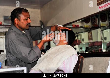 Friseur, der einem Kunden eine traditionelle Rasur in einem Friseursalon in Varanasi, Uttar Pradesh, Indien, gewährt Stockfoto