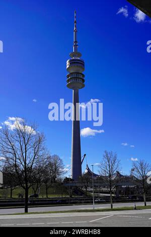 Ein hoher Fernsehturm erhebt sich in den blauen Himmel mit Bäumen im Vordergrund, BMW WELT, München Stockfoto