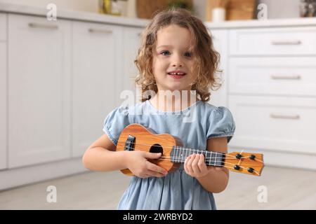 Kleines Mädchen, das Spielzeuggitarre in der Küche spielt Stockfoto