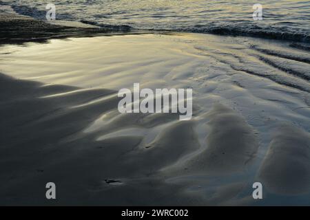 Männer und ein kleiner Junge, der ein großes Boot zurück in die Brandung schiebt Stockfoto