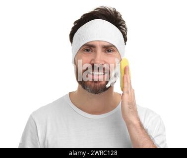 Mann mit Stirnband, der sein Gesicht mit Schwamm auf weißem Hintergrund wäscht Stockfoto