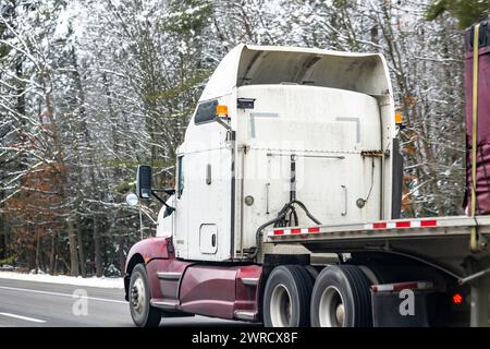 Industrieller Transportwagen Langstreckenfahrzeug mit weißem Big Rig Sattelzugmaschine für den Transport von abgedeckter und befestigter Fracht auf einem Tieflader-Auflieger im Winter Stockfoto